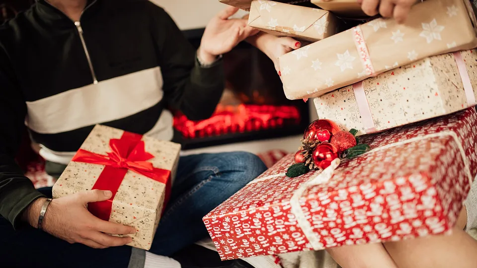Zwei Personen reichen einander eingepackte Geschenke an einem warm beleuchteten Tisch.