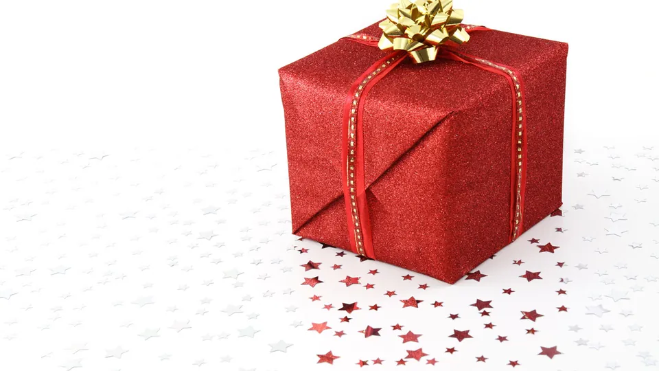Ein kleines rotes Geschenk mit goldener Schleife steht allein auf hellem Untergrund.